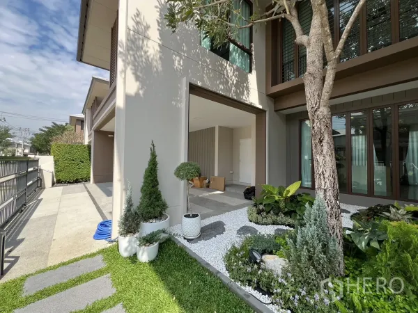 Detached House for rent or sale in Bang Kapi, Bangkok - Side view showing the carport and open-air courtyard with potted plants and lawn.