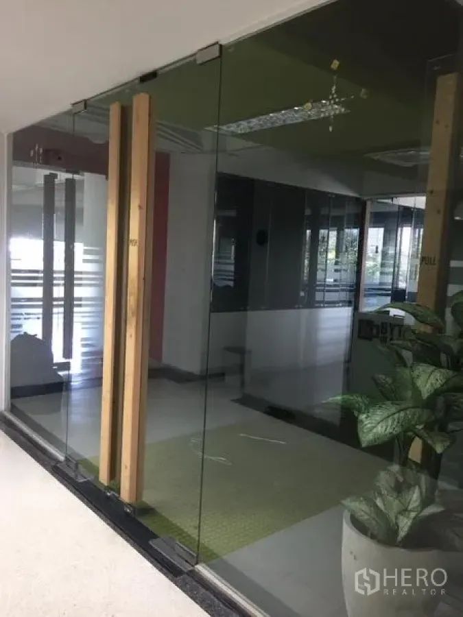 Office Space for rent in Bang Kapi, Bangkok - Modern office entrance with floor-to-ceiling glass doors, timber handles and a potted plant in Bang Kapi.