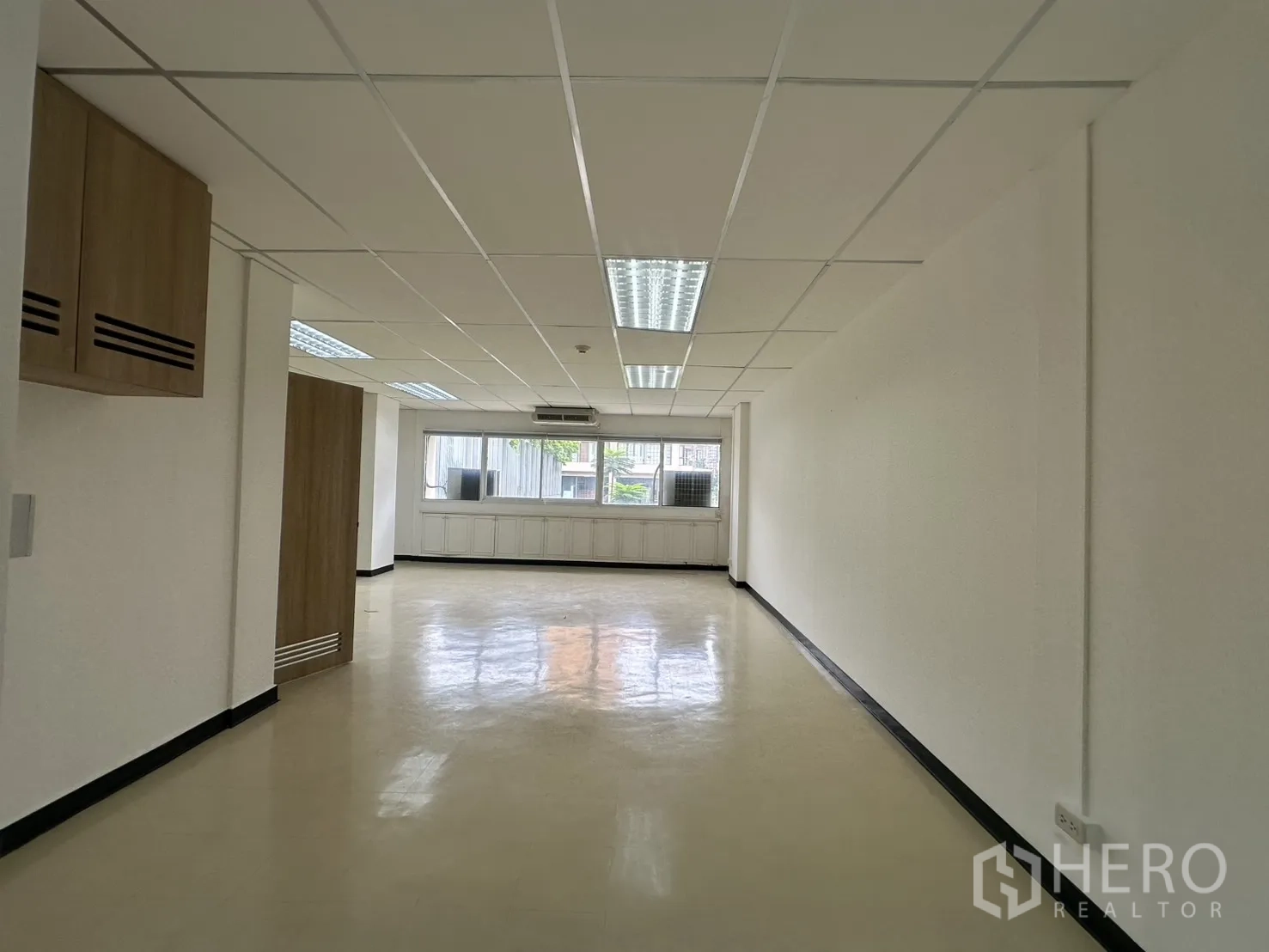 Office Space for rent in Pathum Wan, Bangkok - Narrow open office zone with suspended ceiling lights leading to windows and built-in lower cabinets.