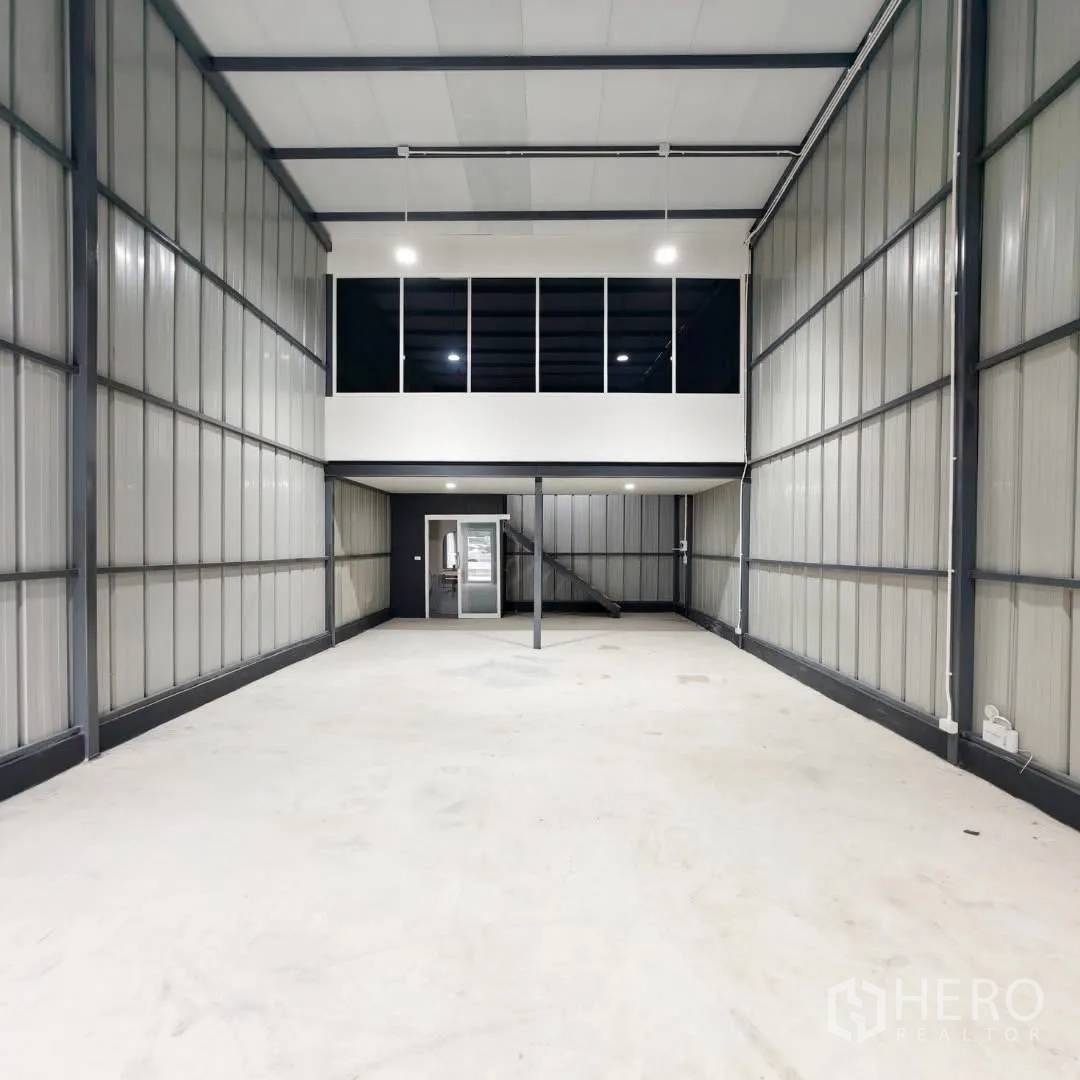 Warehouse for rent in Phra Khanong, Bangkok - High-ceiling warehouse interior with mezzanine glass office and smooth concrete flooring.