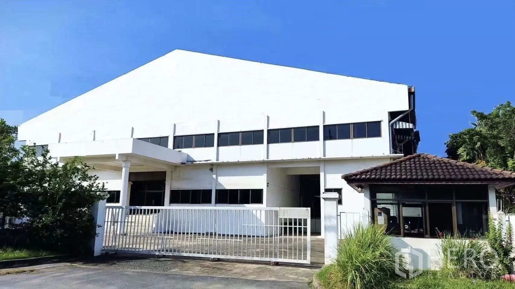 工厂 for sale in Lat Krabang, Bangkok - 白色工厂建筑，带大门与警卫室，蓝天下外观。