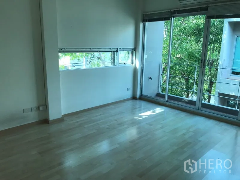 Townhouse for rent in Suan Luang, Bangkok - Corner bedroom with narrow windows and a balcony overlooking greenery.