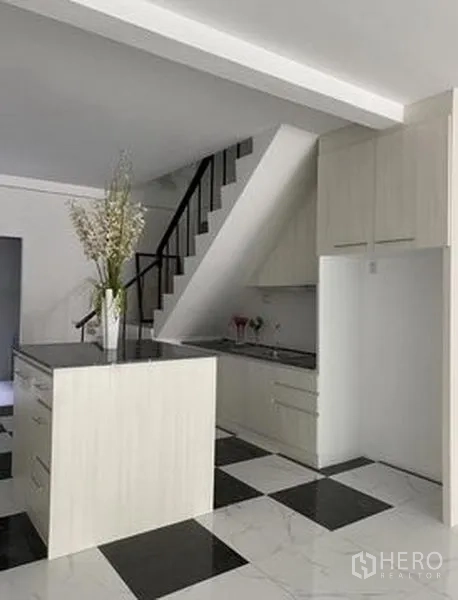 Townhouse for sale in Khlong Toei, Bangkok - Modern under-stair kitchen with white cabinetry and island on glossy checkered tiles.