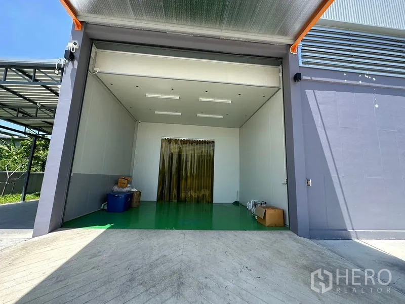 Factory for rent or sale in Lam Luk Ka, Pathum Thani - Loading bay with ramp, roll‑up door and a clean‑room style entrance behind strip curtains.