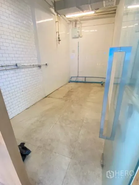 Retail Space for rent in Watthana, Bangkok - View from the glass door into a compact retail space with beige tiles and service piping.