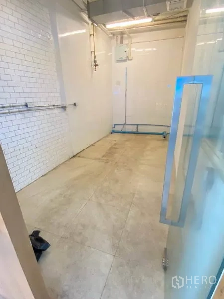 Retail Space for rent in Watthana, Bangkok - View from the glass door into a compact retail space with beige tiles and service piping.