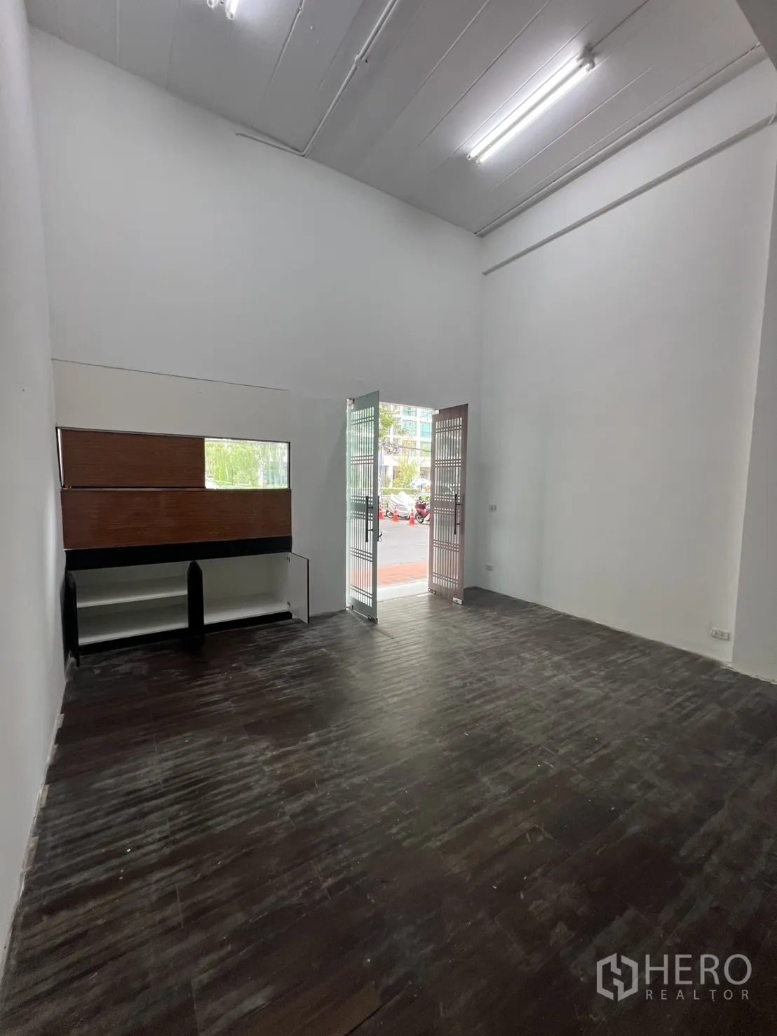 Retail Space for rent in Watthana, Bangkok - Bright front room with tall ceiling, shelving, and gated doors opening to the street.