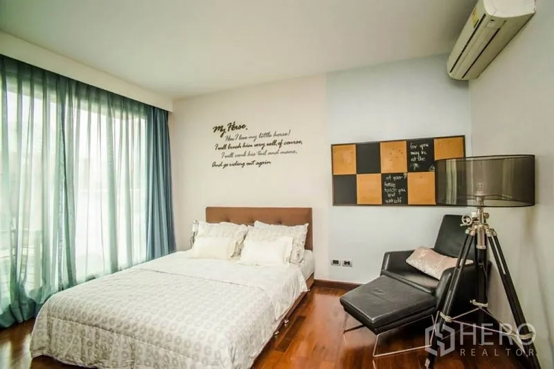 Townhouse for rent or sale in Watthana, Bangkok - Guest bedroom with large windows, sheer curtains and a lounge chair
