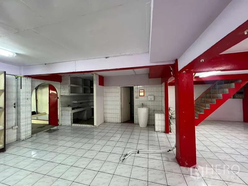 Shophouse for rent in Suan Luang, Bangkok - Retail hall entrance with red columns, stairs and a sink against tiled walls.