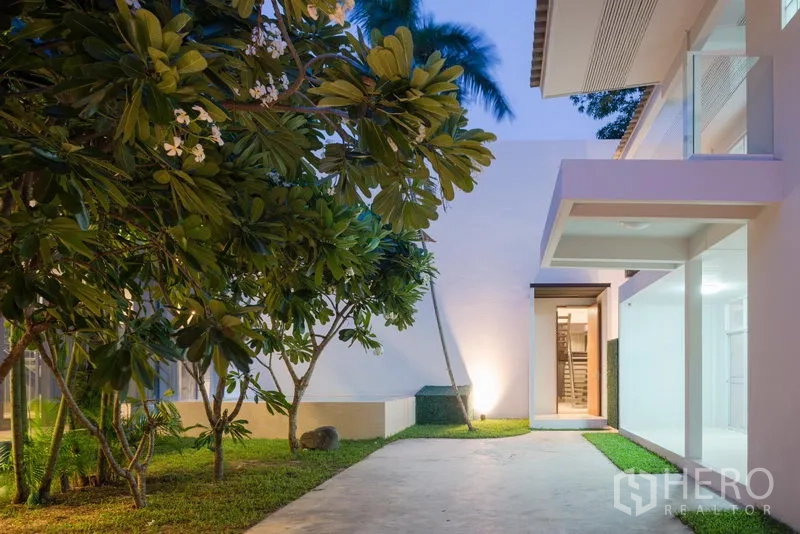 Home Office for rent in Khlong Toei, Bangkok - Landscaped front yard with frangipani trees and a covered entry beside large glass windows.