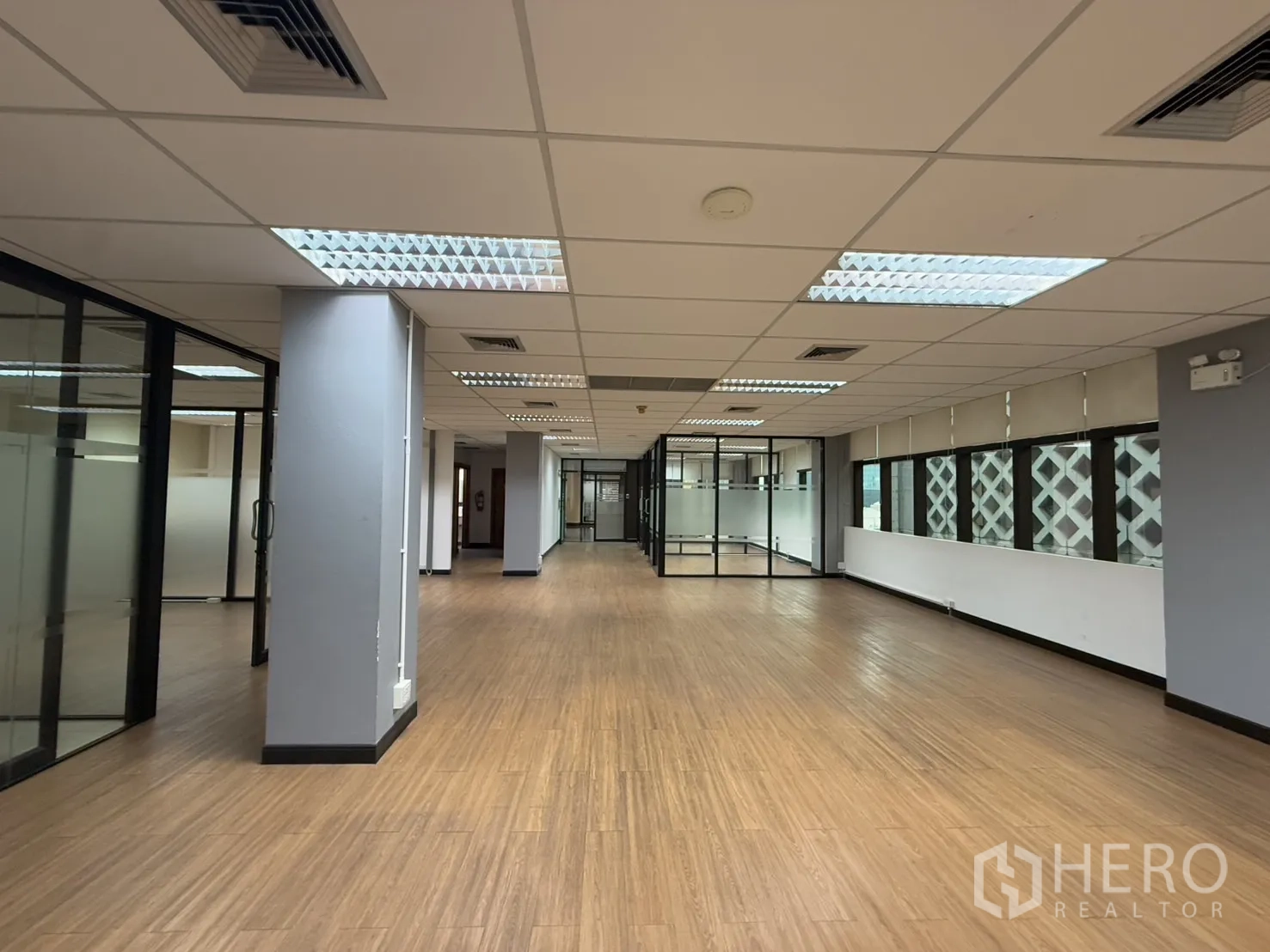 Office Space for rent - Long open-plan office with fluorescent lighting, pillars and glass meeting rooms.