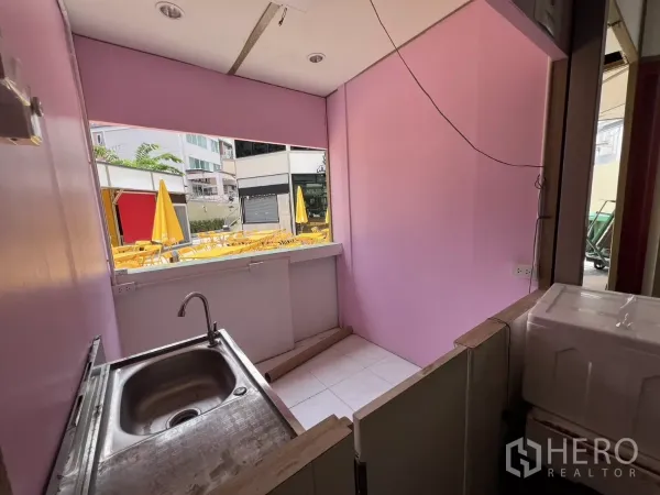 Retail Space for rent in Khlong Toei, Bangkok - Compact service counter with stainless sink and pink walls opening to a courtyard with yellow outdoor umbrellas and seating.