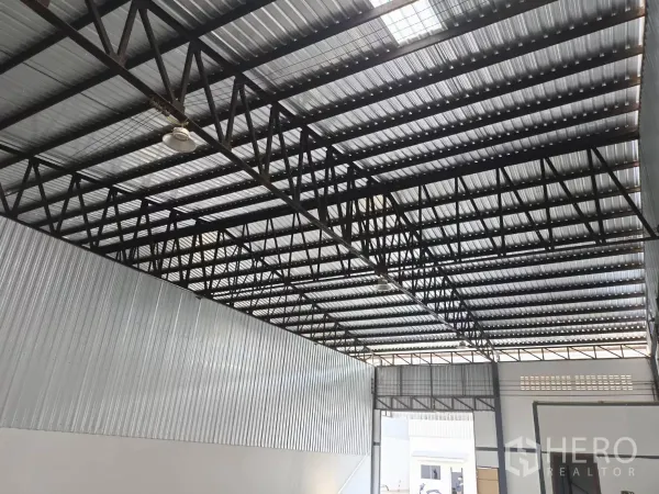 Warehouse for rent in Suan Luang, Bangkok - Metal-sheet roof and steel truss structure with industrial lighting over a wide loading area.