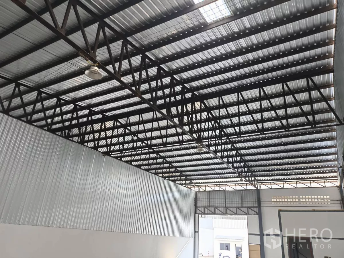 Warehouse for rent in Suan Luang, Bangkok - Metal-sheet roof and steel truss structure with industrial lighting over a wide loading area.