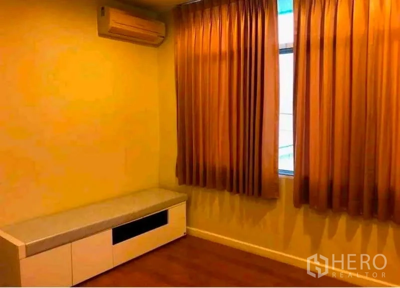 Townhouse for rent in Phra Khanong, Bangkok - Cozy bedroom with orange curtains, air conditioner and a low built-in cabinet.