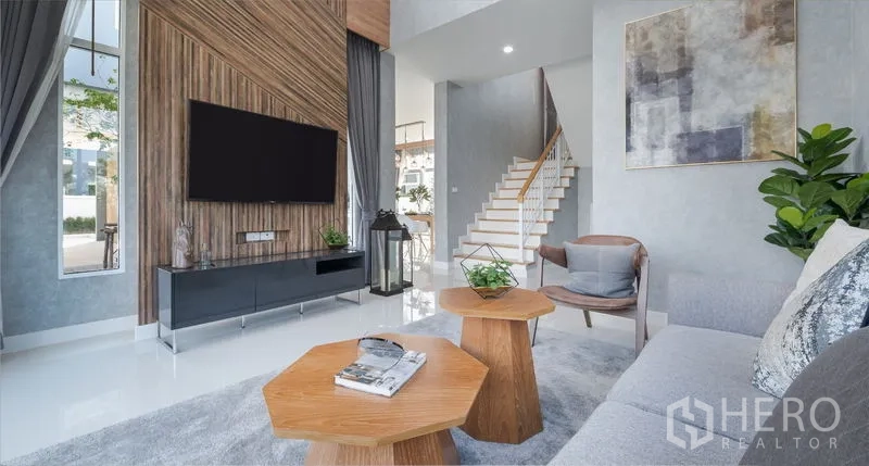Detached House for sale in Lam Luk Ka, Pathum Thani - Double-height living room with feature wall, mounted TV, modern sofa and staircase.