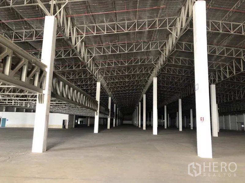 Warehouse for rent in Lam Luk Ka, Pathum Thani - Expansive warehouse interior with high steel truss roof and rows of columns.