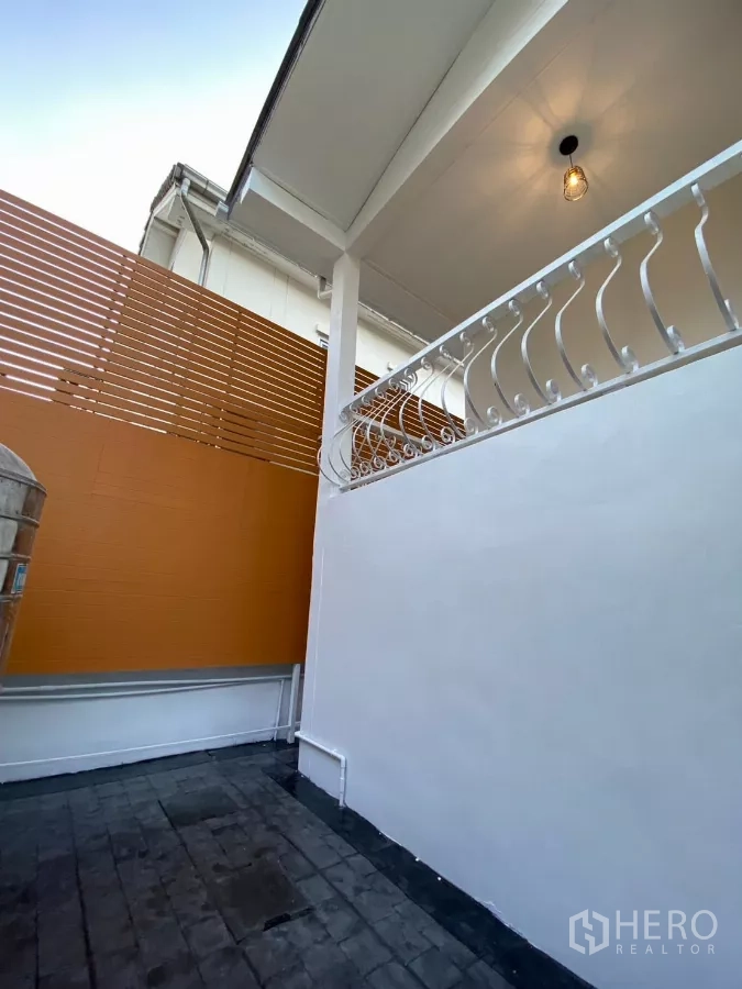 独立式住宅 出租在Bang Na, Bangkok - 房屋侧院，白色栏杆、高隐私围挡与铺装地面。