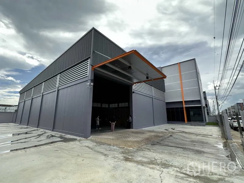工厂 出租或出售在Lam Luk Ka, Pathum Thani - 工厂外立面的大型卷闸门与带顶装卸区。