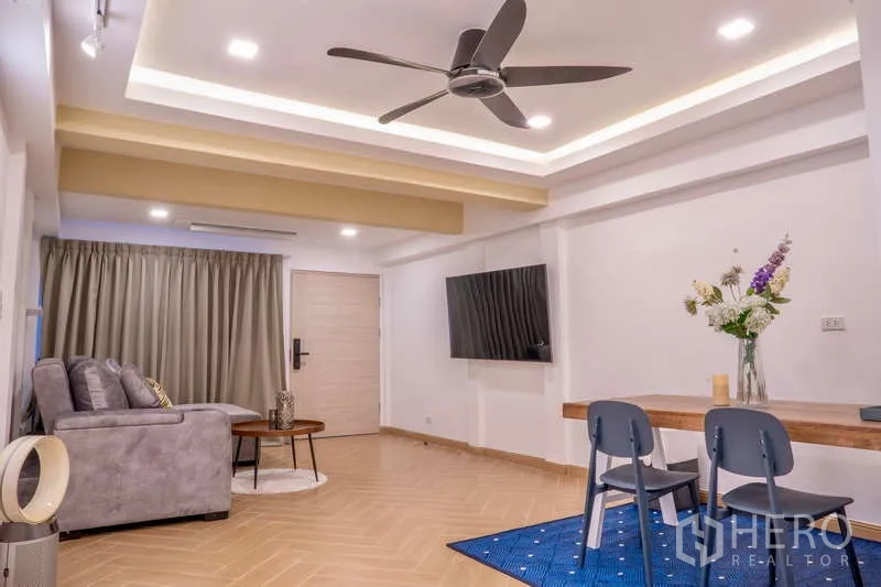 Townhouse for rent in Khlong Toei, Bangkok - Spacious living room with ceiling fan, mounted TV and dining set.