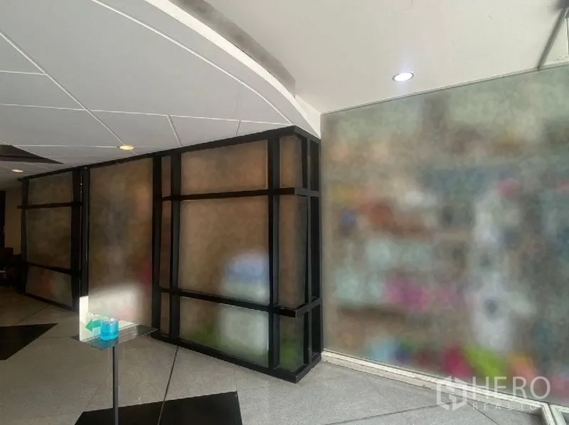 Retail Space for rent in Watthana, Bangkok - Interior corridor view showing black-framed glass partitions and curved white ceiling near a retail entrance.
