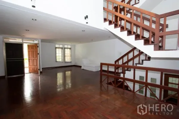 Townhouse for rent in Khlong Toei, Bangkok - Spacious living room with polished parquet floors and open wooden staircase.
