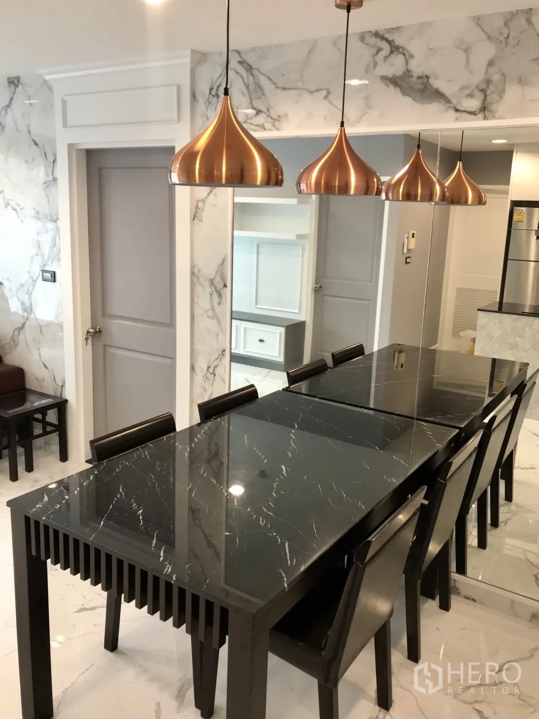 Condominium for rent or sale in Khlong Toei, Bangkok - Dining area with long black glass table, six chairs and trio of copper pendant lights by a mirror wall.