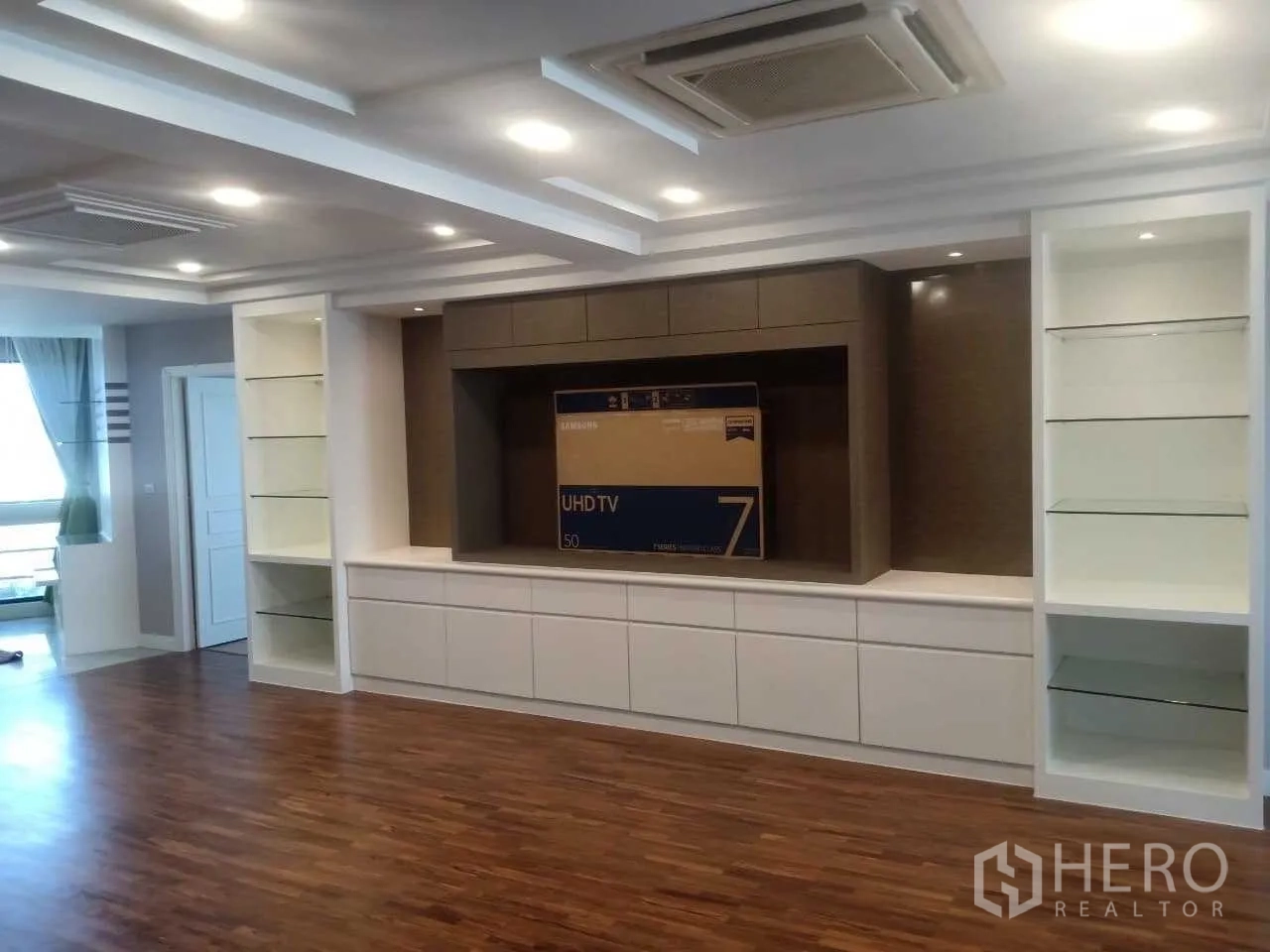 Condominium for rent in Khlong Toei, Bangkok - Built-in TV wall with glass display shelves and wood floors in the living space.