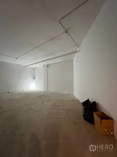 零售空间 出租 - 店铺角落视角，白色墙面、天花管道与抬高地面。