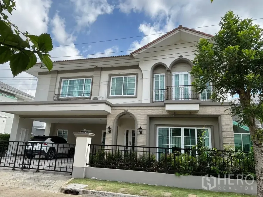Detached House for rent in Prawet, Bangkok - Two-storey detached house with gated fence, balcony and covered carport set in a landscaped front yard.