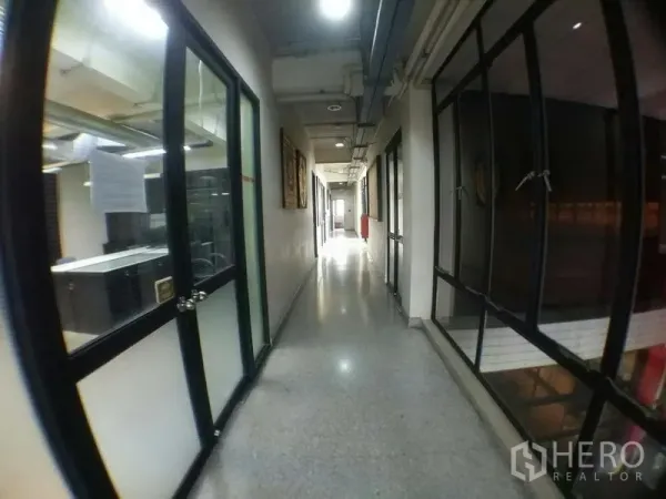 办公空间 出租在Phra Khanong, Bangkok - 明亮走廊，两侧玻璃隔间办公室与外露管线天花。