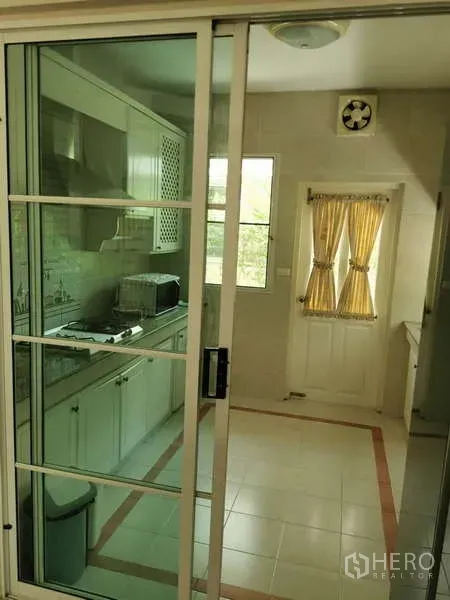 Detached House for rent - Separate enclosed kitchen behind a glass sliding door with white cabinets, cooktop, and a window with yellow curtains.