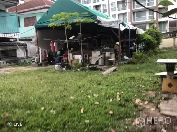 地 出售在Phra Khanong, Bangkok - 地块内的草地空地，带临时帐篷结构，后方为中高层公寓。