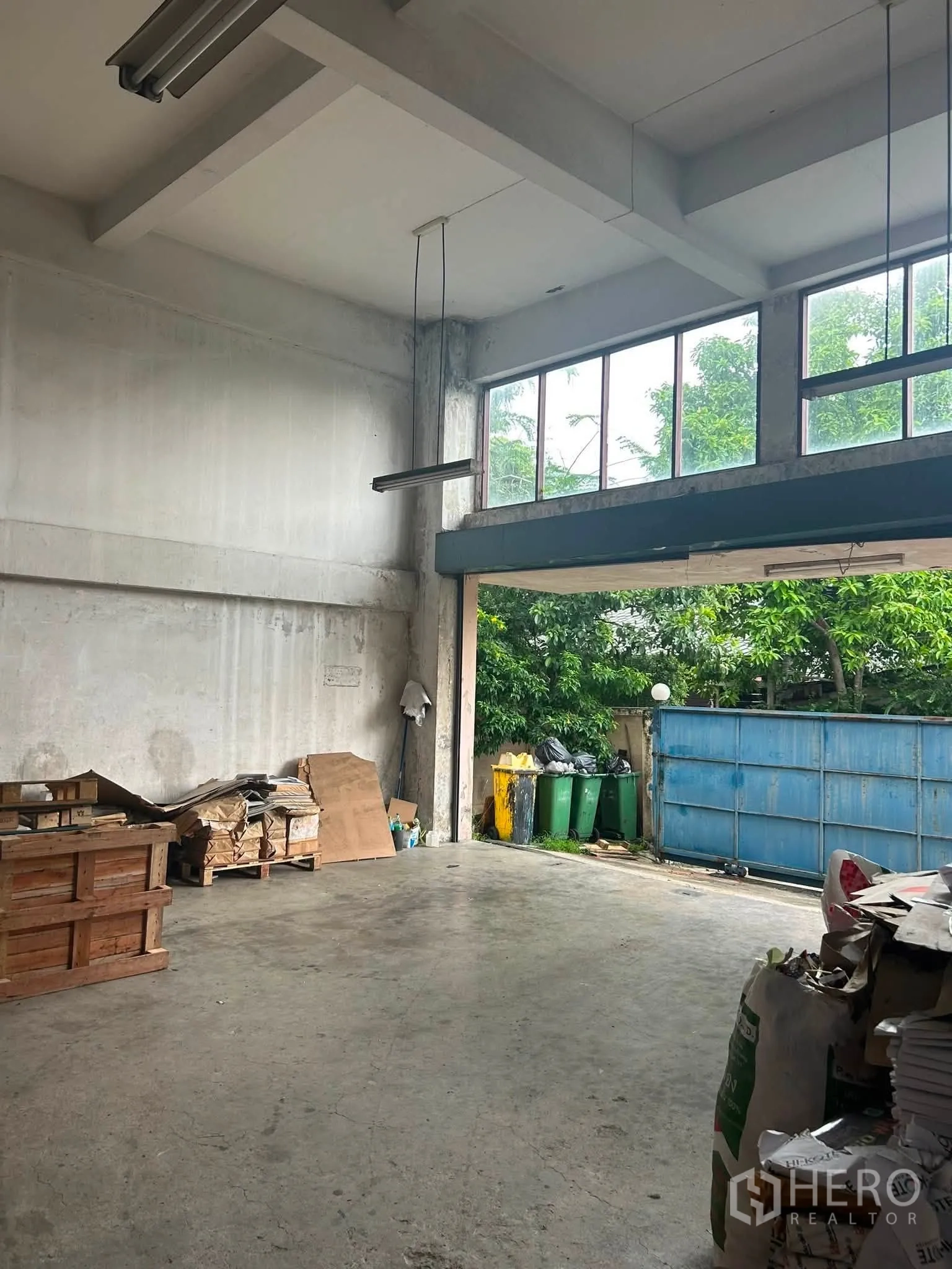 Warehouse for rent in Phra Khanong, Bangkok - Ground-level loading area with high ceiling, tall windows, and a wide metal gate opening to the yard.