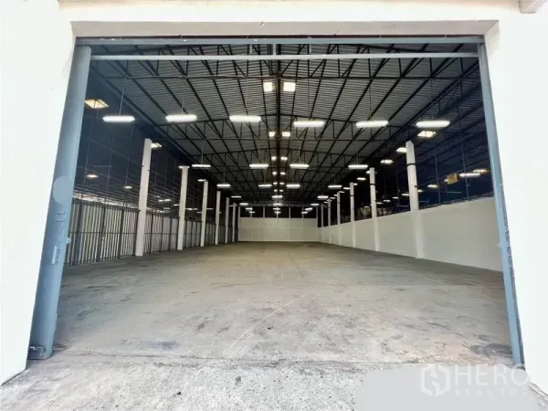 Warehouse for rent in Pak Kret, Nonthaburi - Open warehouse interior with high-clearance steel truss ceiling, bright LED lights, white columns and polished concrete floor.