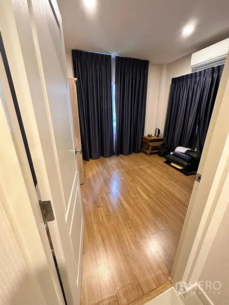 Detached House for sale in Prawet, Bangkok - Bedroom viewed from doorway with wood flooring, dark drapes and A/C.