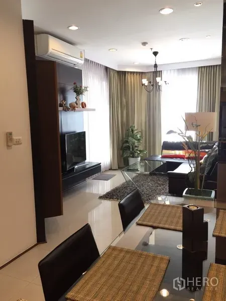 Condominium for rent in Khlong Toei, Bangkok - Dining table facing a bright living room with large windows and chandelier lighting.