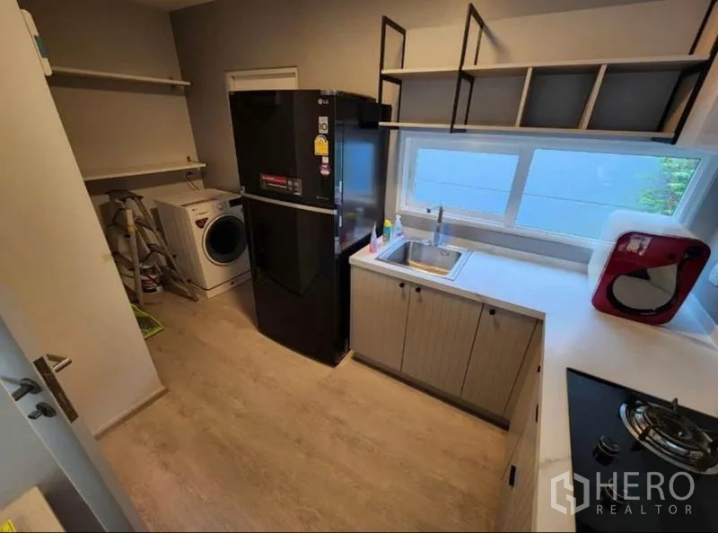 Detached House for rent in Prawet, Bangkok - Modern separate kitchen with window, sink, gas hob, refrigerator, open shelves, and washing machine.