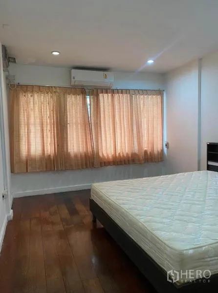 Townhouse for rent in Khlong Toei, Bangkok - Bedroom with wooden flooring, curtains, and a split-type air conditioner above the window.