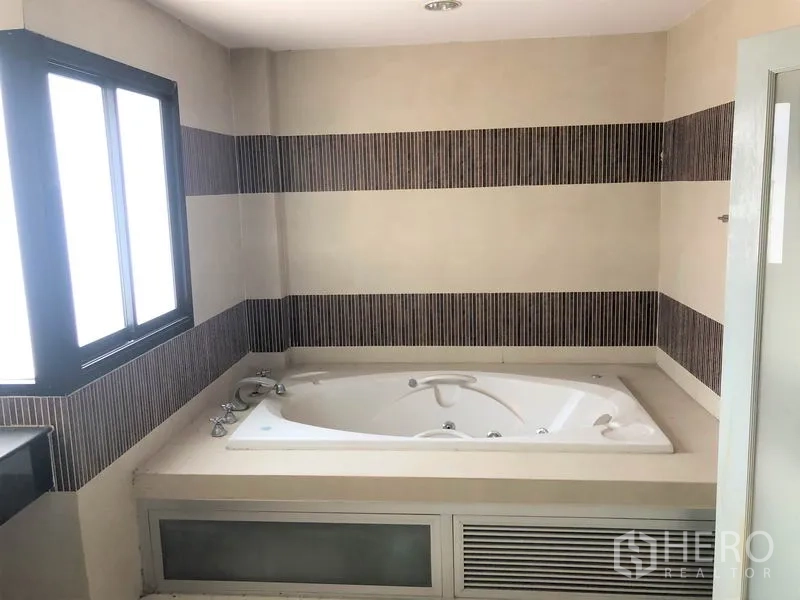 Home Office for rent in Wang Thonglang, Bangkok - Bathroom featuring a built-in Jacuzzi bathtub, striped wall tiles and a frosted window.