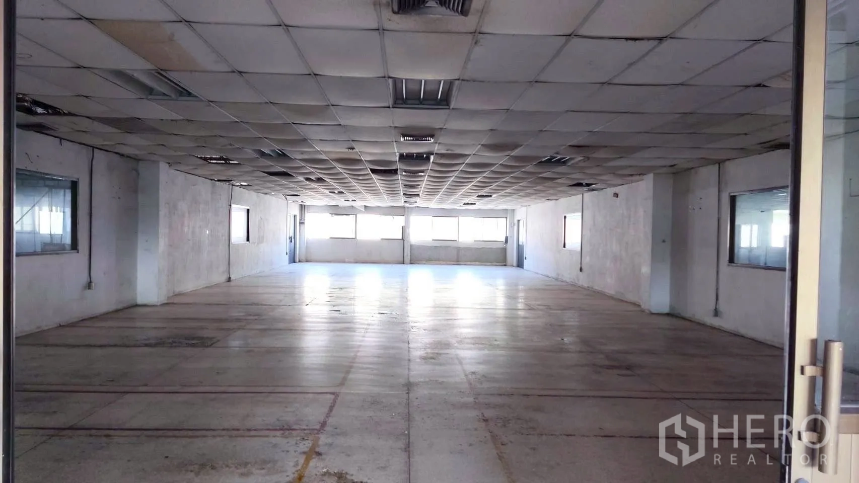 Factory for sale in Lat Krabang, Bangkok - Spacious hall with drop ceiling tiles, strip lighting, and windows at the end wall.
