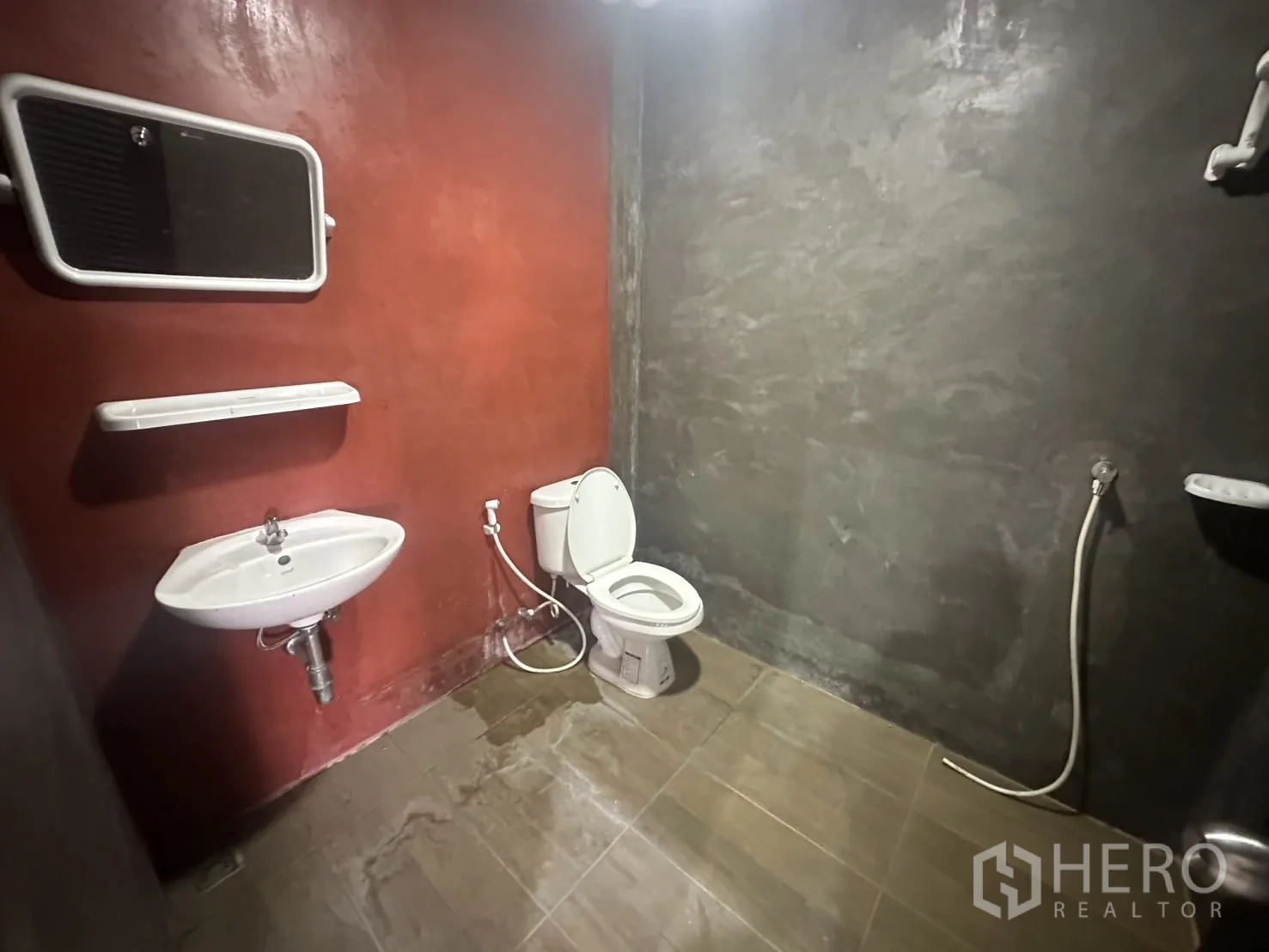 Warehouse for rent in Prawet, Bangkok - Simple bathroom with toilet, sink, mirror and handheld bidet against concrete-finish walls.
