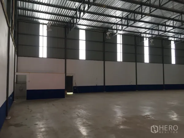 货栈 出租在Pathum Thani - 仓库内部一角，设有高竖向窗及小型办公/卫生间区域。