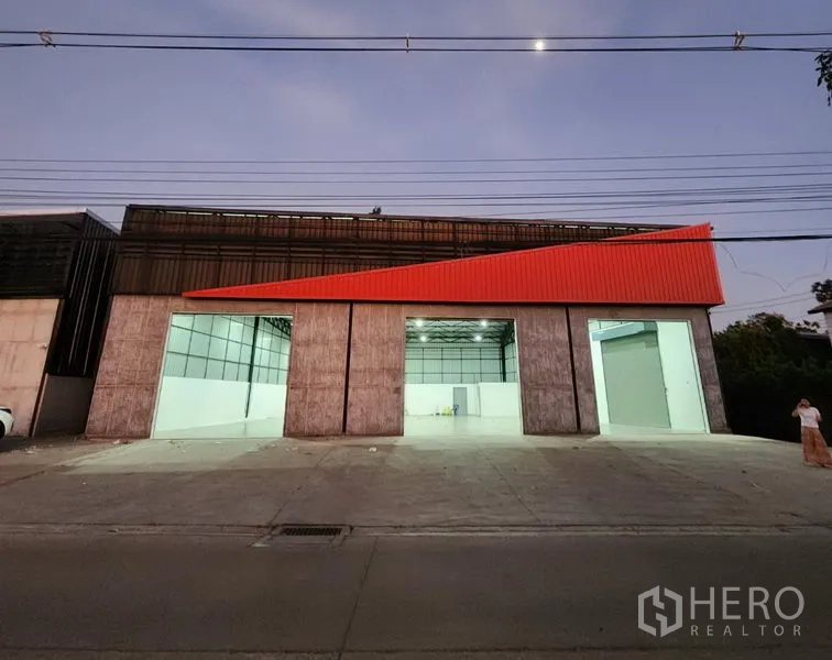 货栈 出租在Pak Kret, Nonthaburi - 傍晚外景，开启的装卸口可见明亮的高顶仓库内部。