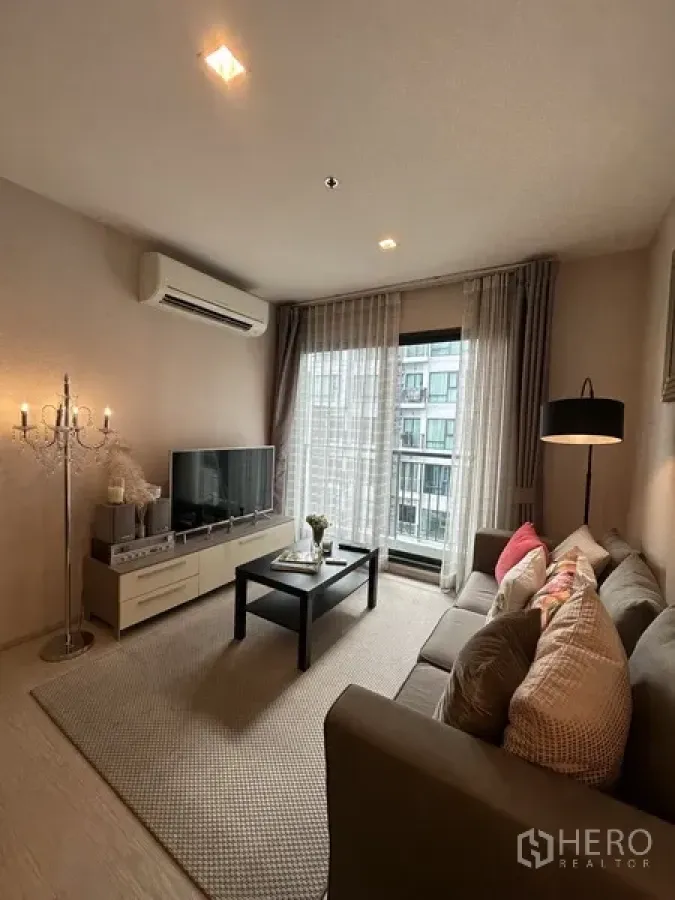 Condominium for rent or sale in Khlong Toei, Bangkok - Living area with TV, air conditioner, coffee table, and sliding glass door to balcony.