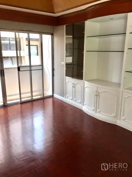 Townhouse for rent in Watthana, Bangkok - Room with built-in white display cabinet, polished wood floors and balcony access.