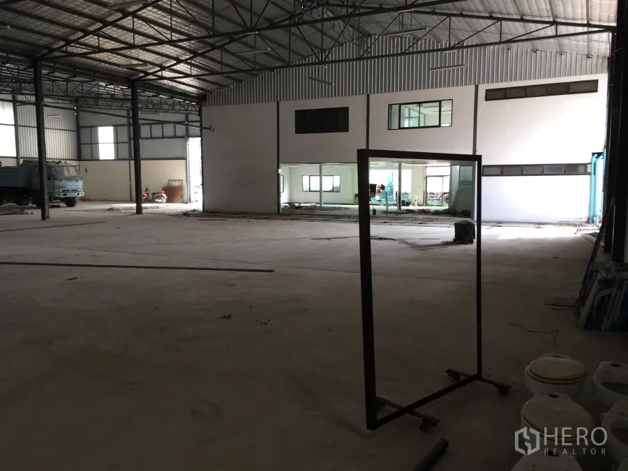Warehouse for rent in Saphan Sung, Bangkok - Spacious warehouse interior with high steel trusses, concrete floor, and a built-in office block with glass windows.