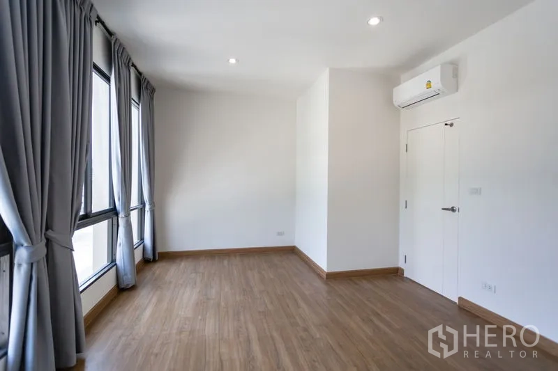 Townhouse for rent in Bang Phli, Samut Prakan - Sunlit bedroom with tall windows, grey curtains and a split-type air conditioner.