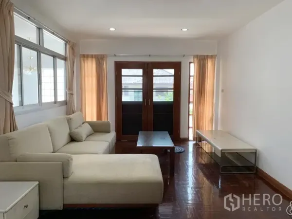 Detached House for rent in Khlong Toei, Bangkok - Bright living room with cream L-shaped sofa, wooden French doors and polished hardwood floors.