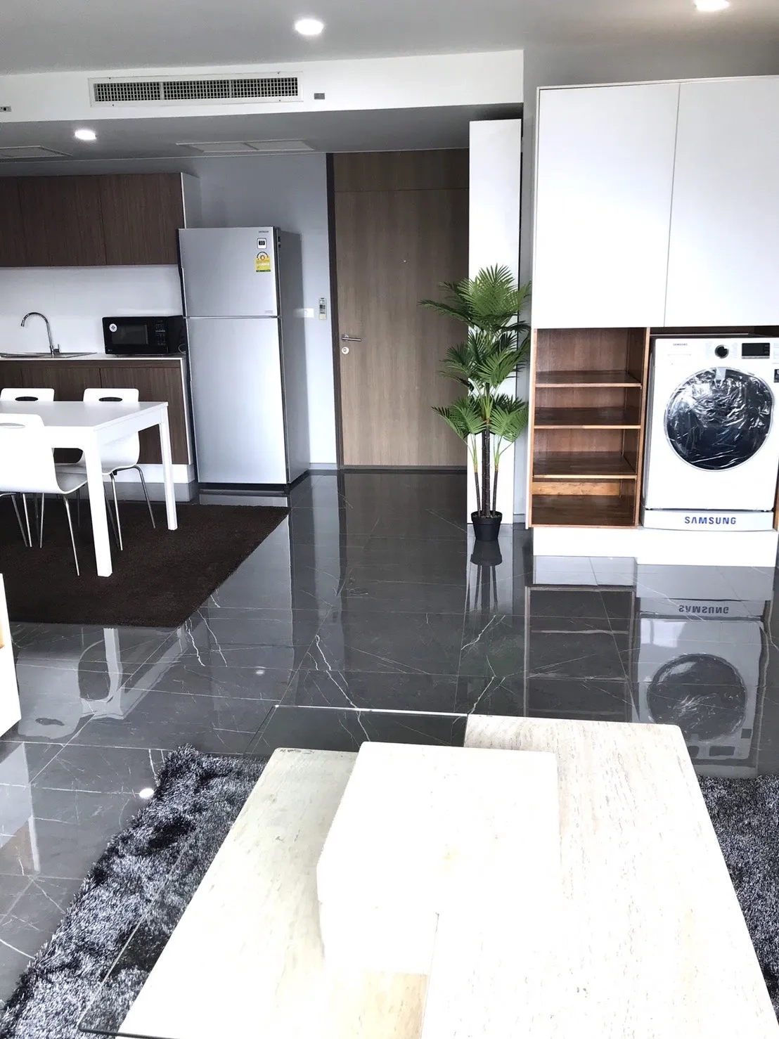 Condominium for rent in Khlong Toei, Bangkok - Entry and kitchen area with glossy floors and a built-in washer-dryer niche.